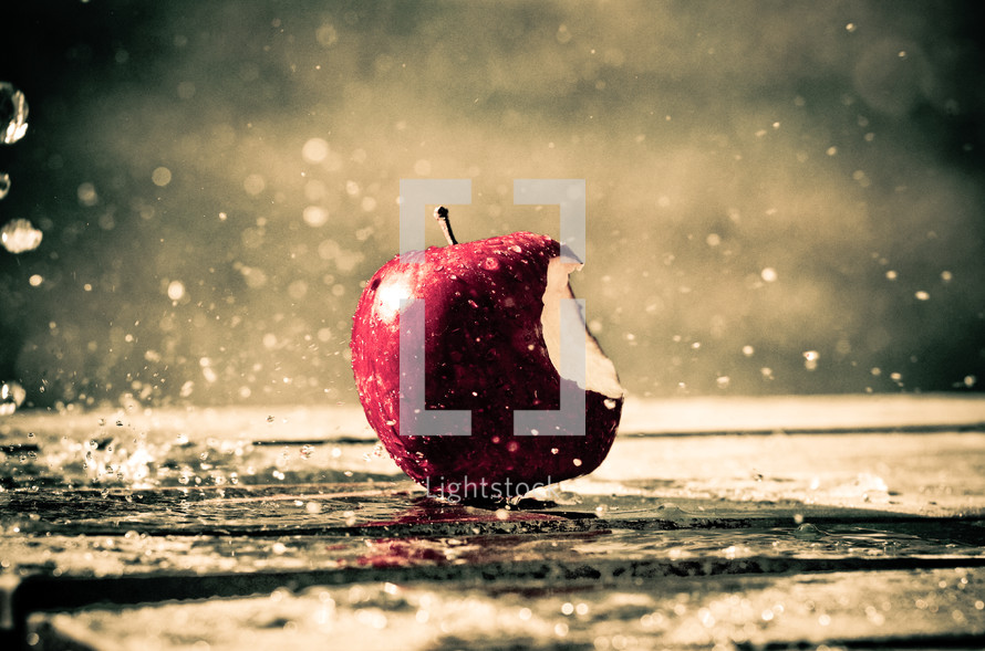 rain falling on an apple with a bite out of it
