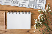 pencil, notepad, white flowers, and computer keyboard on a desk 