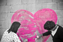 Couple painting a heart on a brick wall.