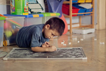 Asian boy child coloring on a chalkboard with chalk 