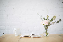 vase of flowers, open Bible, and coffee cup on a table 