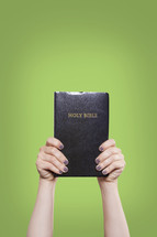 woman holding up a Bible in the air against a green background