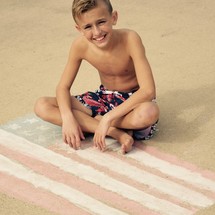a boy child in a bathing suit sitting on an American flag in sidewalk chalk 