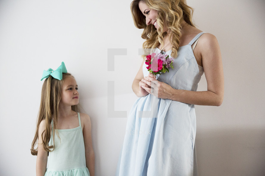 A mother holding flowers and smiling at her young daughter.