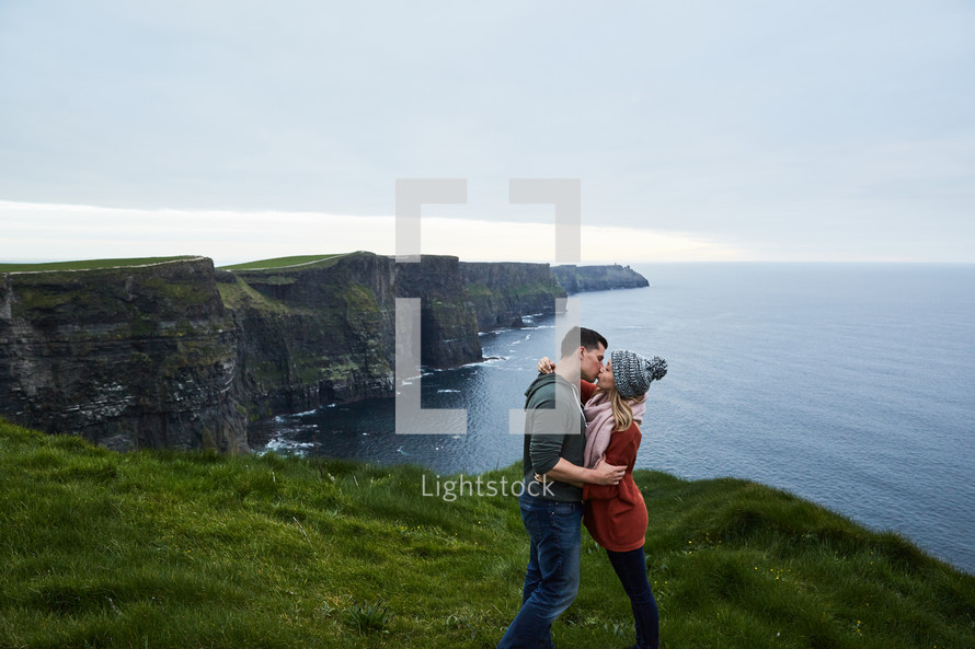 a couple kissing at the edge of a sea cliff 