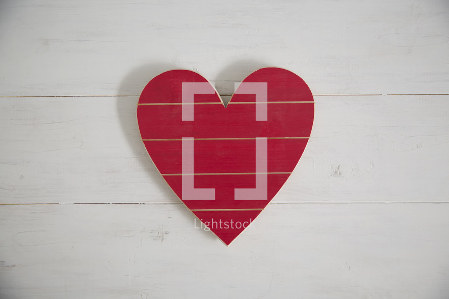 A red wooden heart on a white wood background.