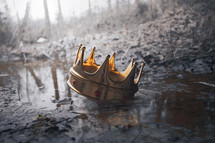 A crown thrown down to the ground rests in a muddy stream
