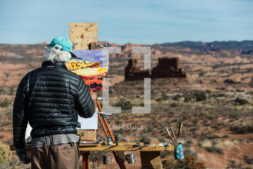 artist painting on canvas outdoors by a canyon