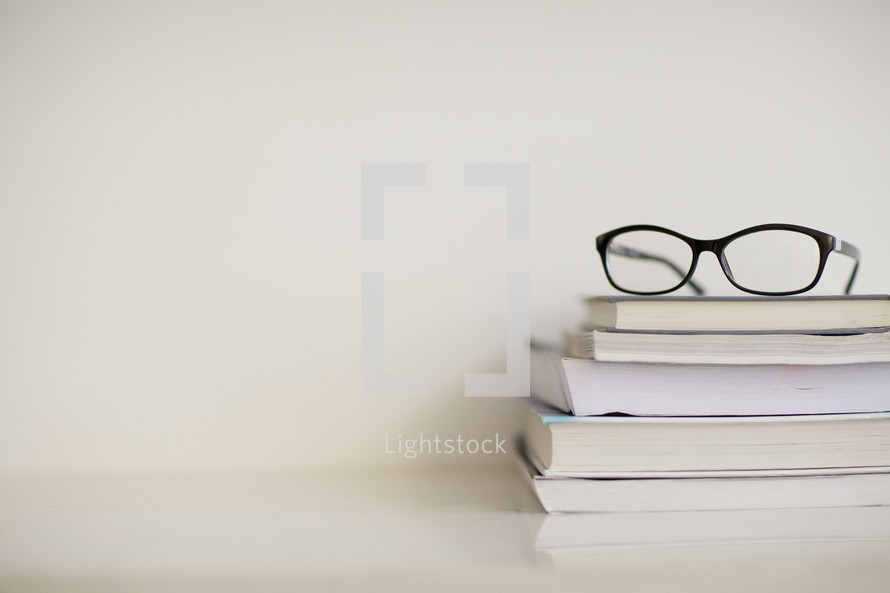 A pair of black eyeglasses on top of a stack of books.