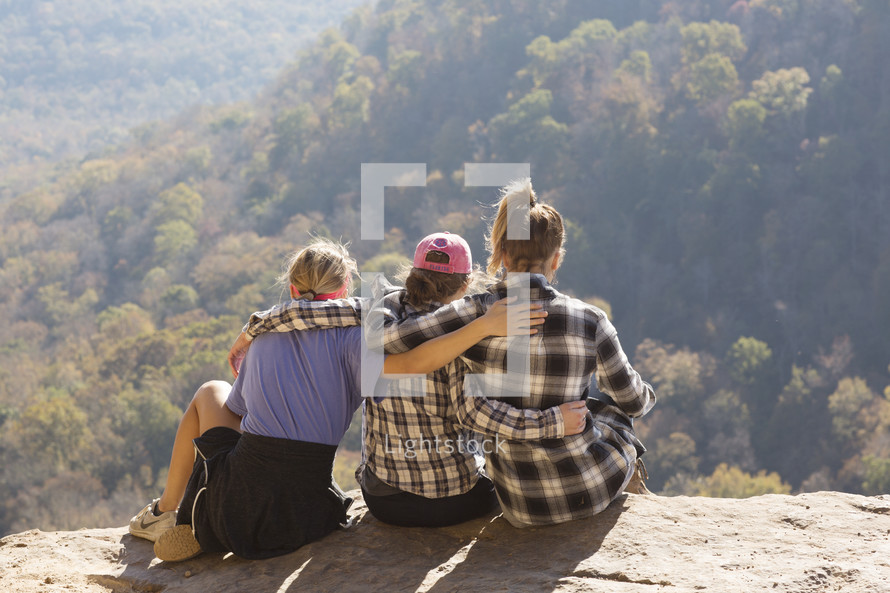 friends embracing sitting with legs hanging over a cliff 