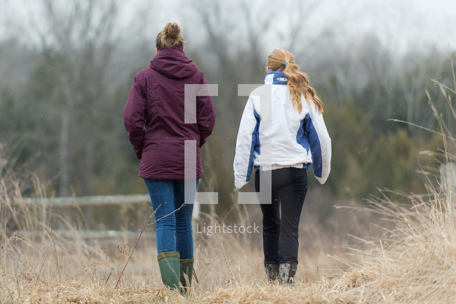 Two women in coats walking in the countryside.
