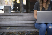 a young woman sitting on a bench with a laptop on her lap 