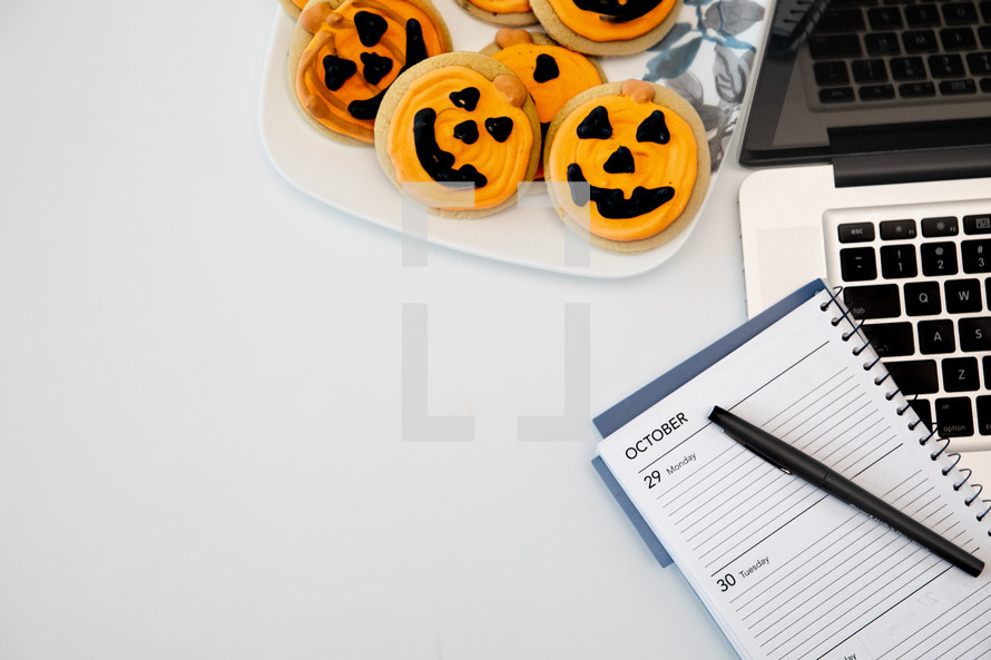 Halloween cookies on a plate next to a laptop computer 