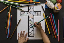 a boy coloring a cross coloring page 