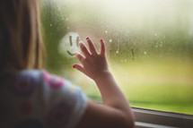 a child drawing a smiley face on a steamed up window 