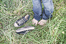 Young girl barefoot in the tall grass with sneakers.