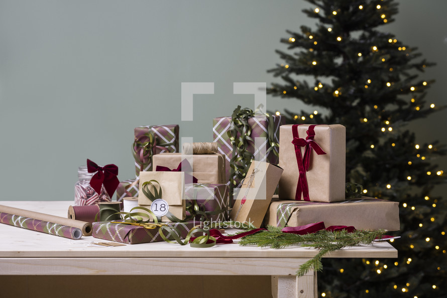 Festive Christmas Stock Photos: Presents on a Table, Some Wrapped, Some Unwrapped, Featuring a Christmas Tree in the Background and a Pristine Wall