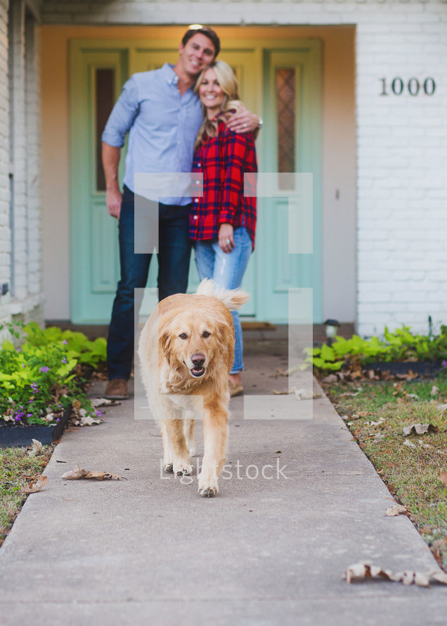 happy couple and their dog in front of their home 