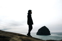 silhouette of a man standing on a rocky beach 