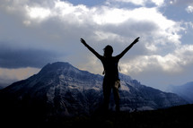 silhouette of a woman with raised arms on a mountain 