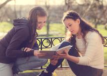 teen girls reading a journal together outdoors 