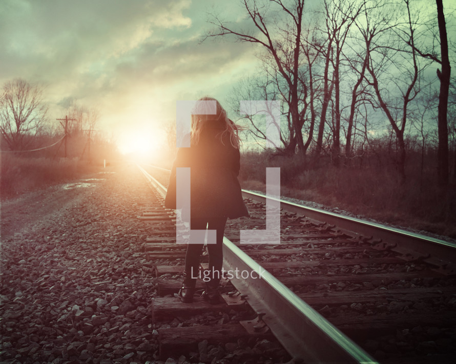 a girl walking on railroad tracks 