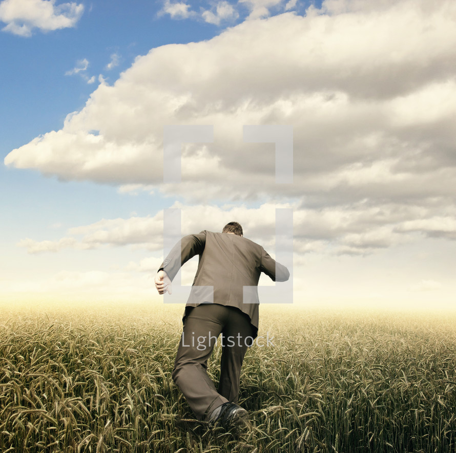 a man in a suit running through a field of wheat 