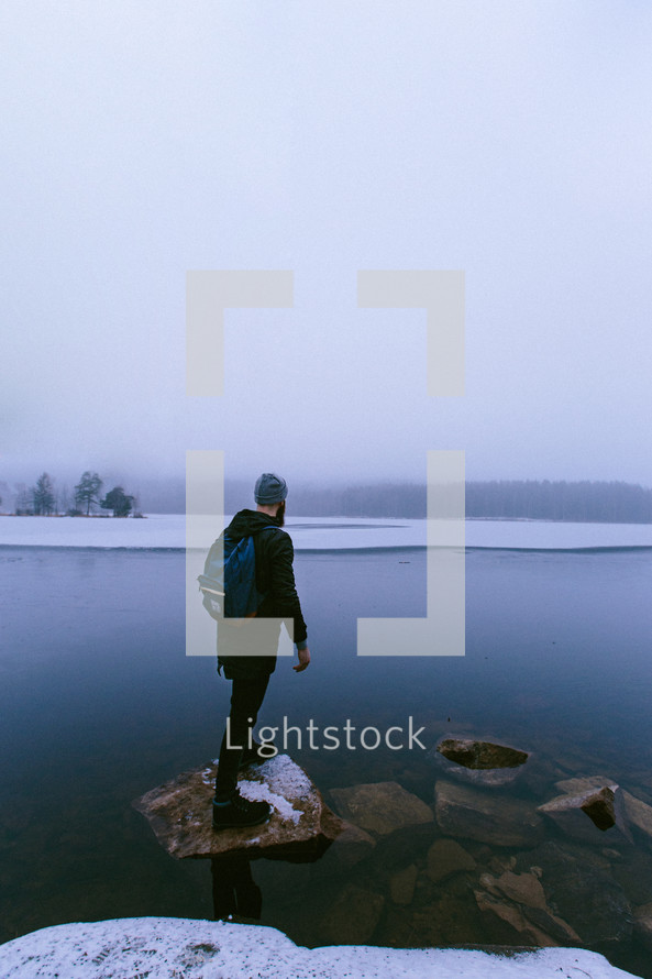 Man standing on a rock at the edge of an icy lake