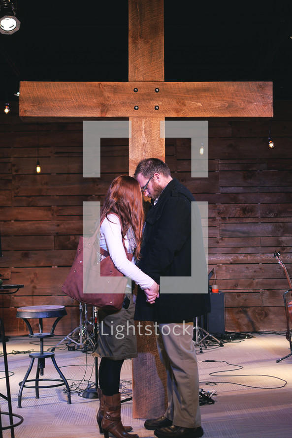 a couple holding hands praying in front of a cross 