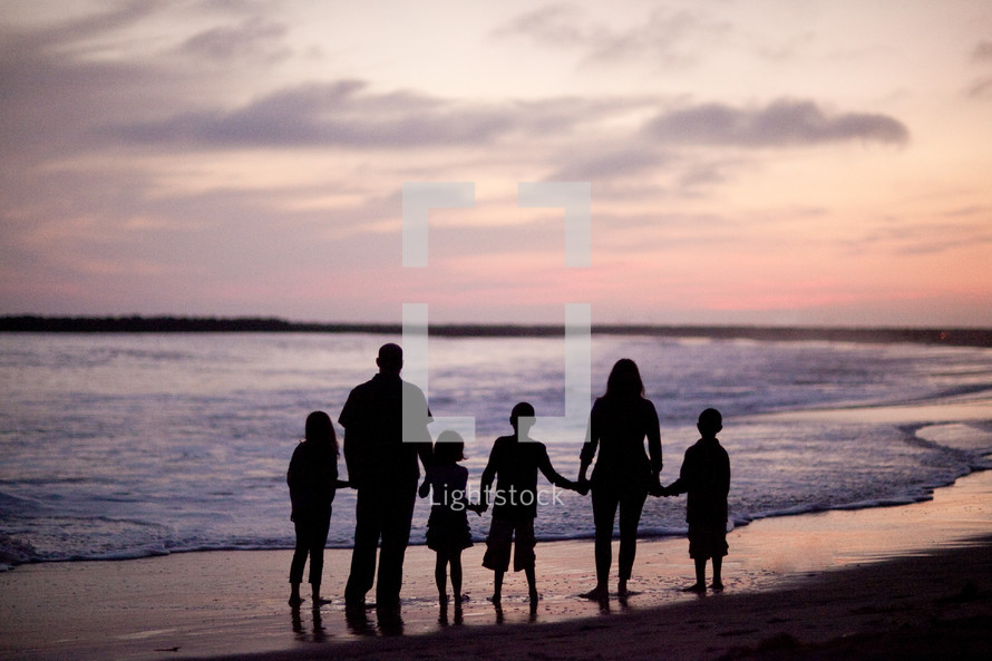 A family of six standing on a beach silhouetted against the sunset