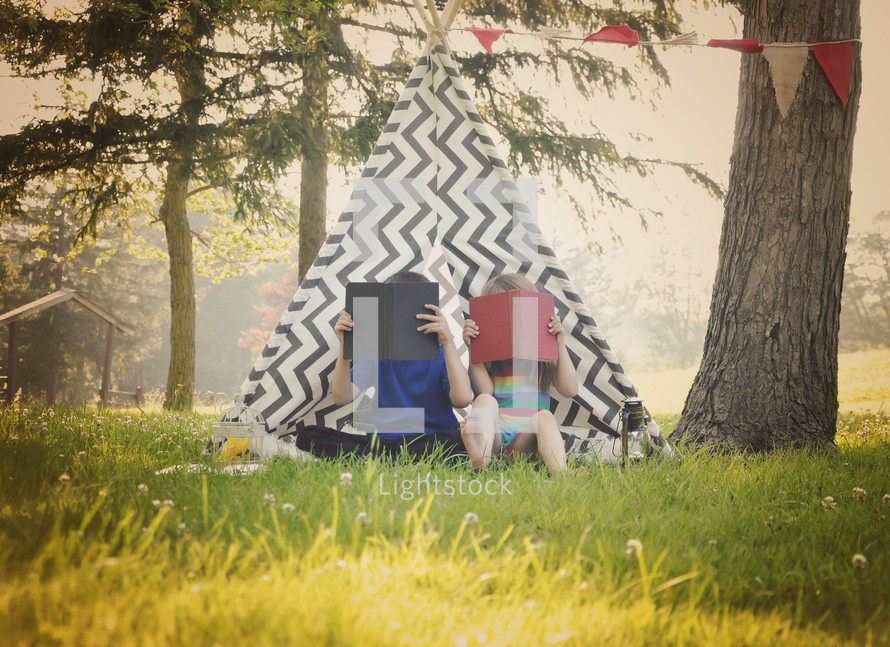 children reading outdoors in front of a teepee 