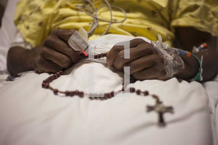 A person in a hospital bed holding a string of rosary beads.