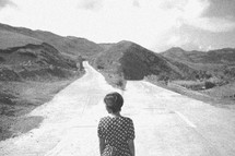 A woman standing in the middle of a road that divides into two directions.