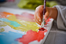 A child paints with colorful paints on a canvas.