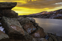 The sky bursts with color on Horsetooth Reservoir with graffiti on the boulders overlooking the lake