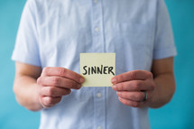 a man holding a piece of paper with the word sinner 