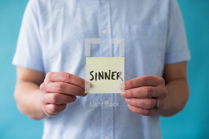 a man holding a piece of paper with the word sinner 