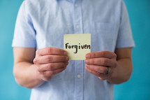 man holding a piece of paper with word forgiven 