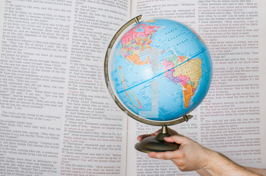 Hands holding globe in front of open pages of the Bible.