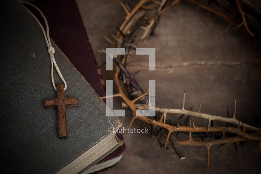 cross necklace on a stack of books and crown of thorns 