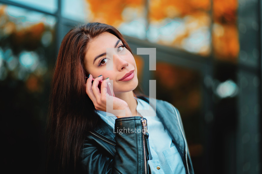 Business woman with smartphone close up in autumn city, sunset light. Girl have conversation with cell phone. Beautiful caucasian young woman talking with mobile device.