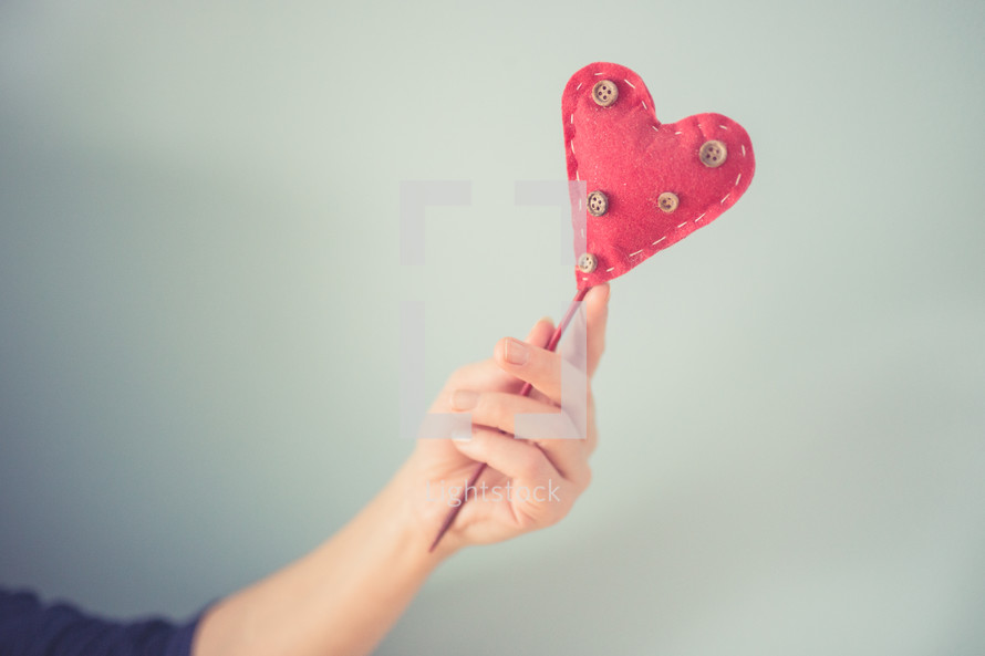 woman holding up a felt heart on a stick 