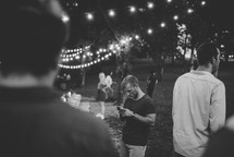 A man looking at his cell phone at an outdoor dinner party.