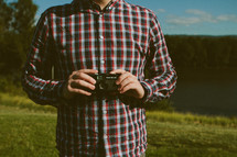 torso of a man in a plaid shirt holding a camera 