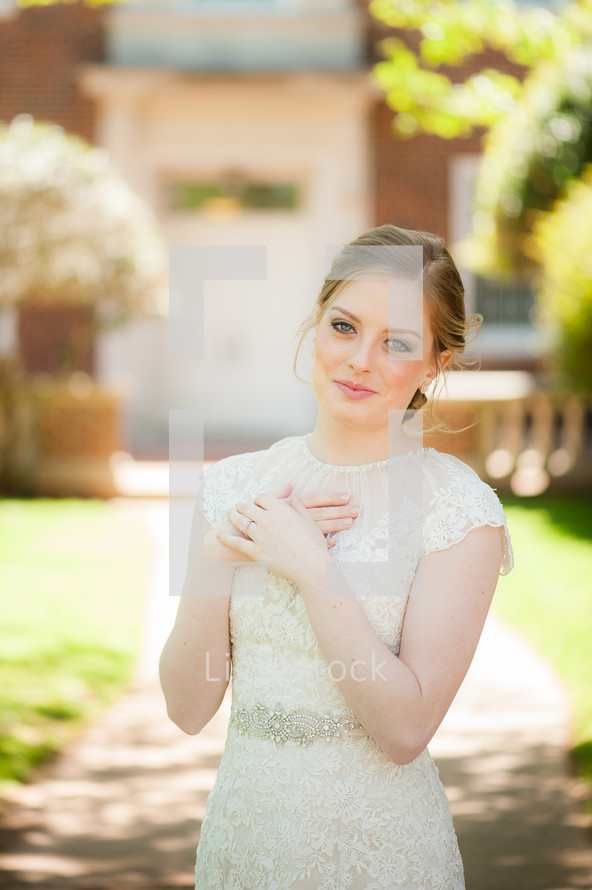 a bride in a lace gown with hands over her heart 