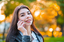 Business woman with smartphone close up in autumn city, sunset light. Girl have conversation with cell phone. Beautiful caucasian young woman talking with mobile device.