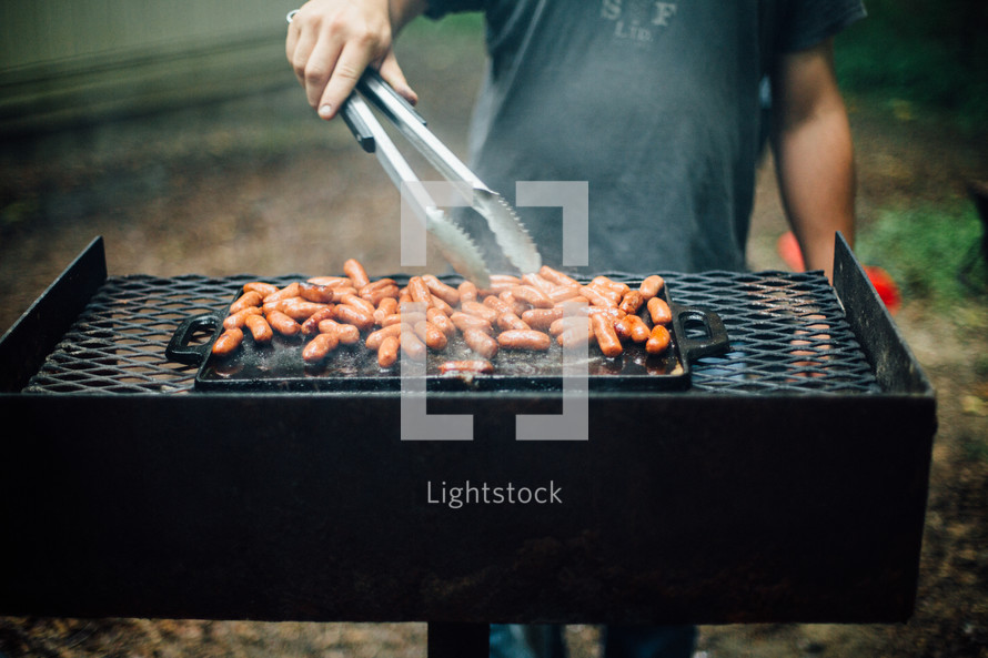 flipping hotdogs on a grill 