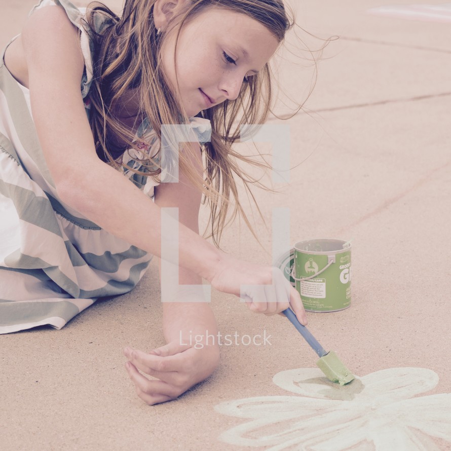 a little girl painting a green clover with sidewalk chalk paint for St Patrick's Day