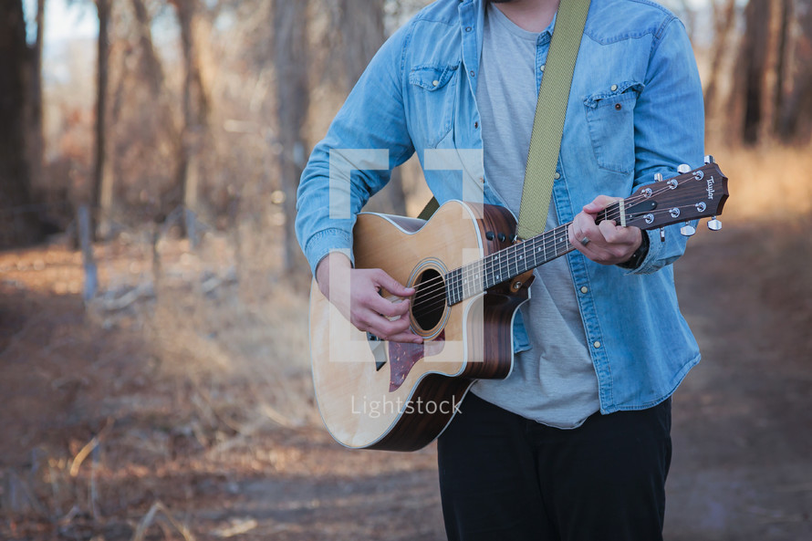 man standing outdoors holding an acoustic guitar 