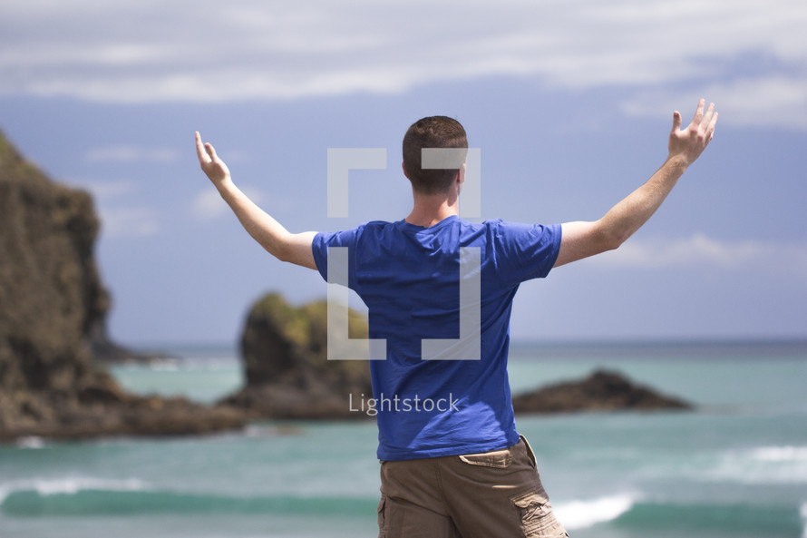man with raised hands standing on a beach 